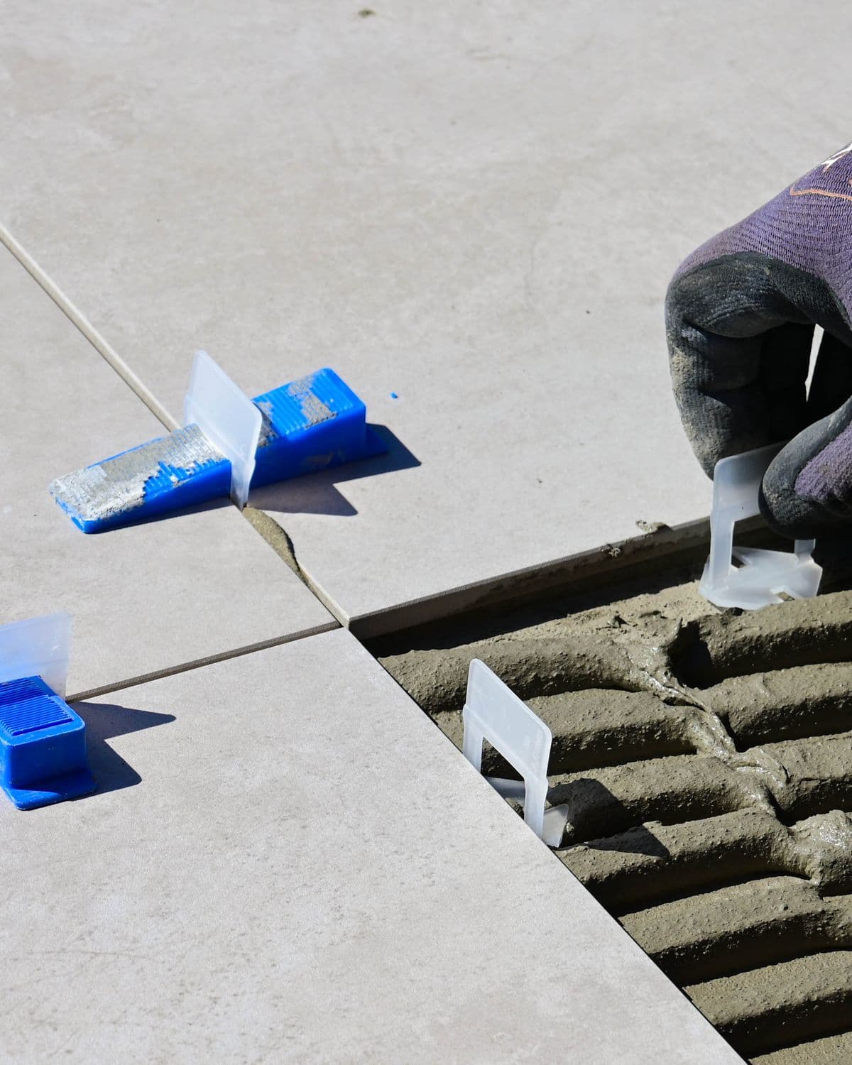 Gloved hands setting floor tile into notched thinset with leveling spacers, showing careful alignment.